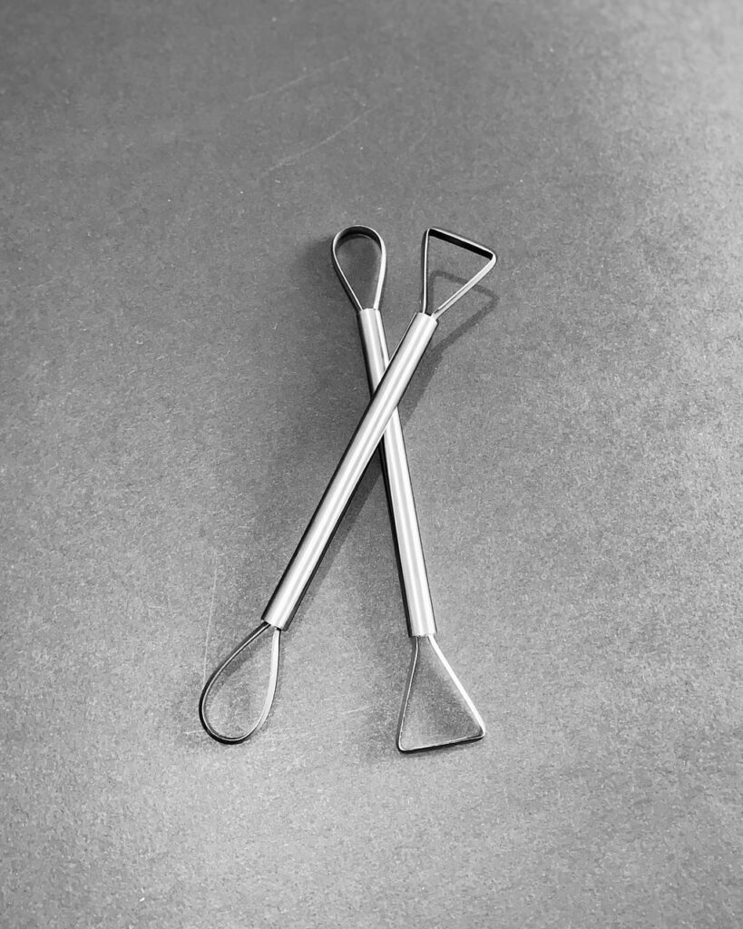 A DOUBLE ENDED TRIMMING TOOL, ONE WITH A TRIANGLE & A ROUND END.